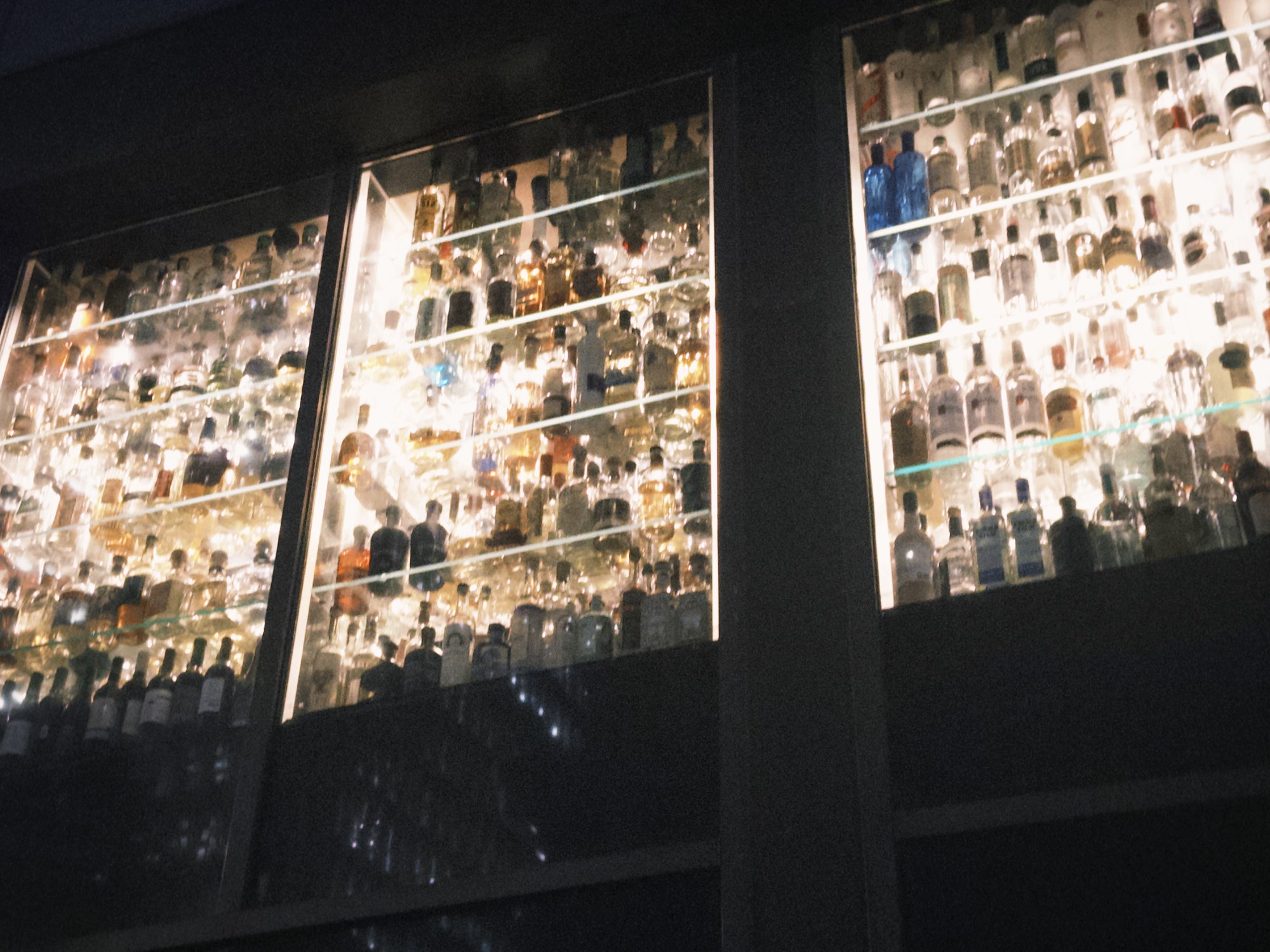 Backlit bottles in a waterfront bar at night.