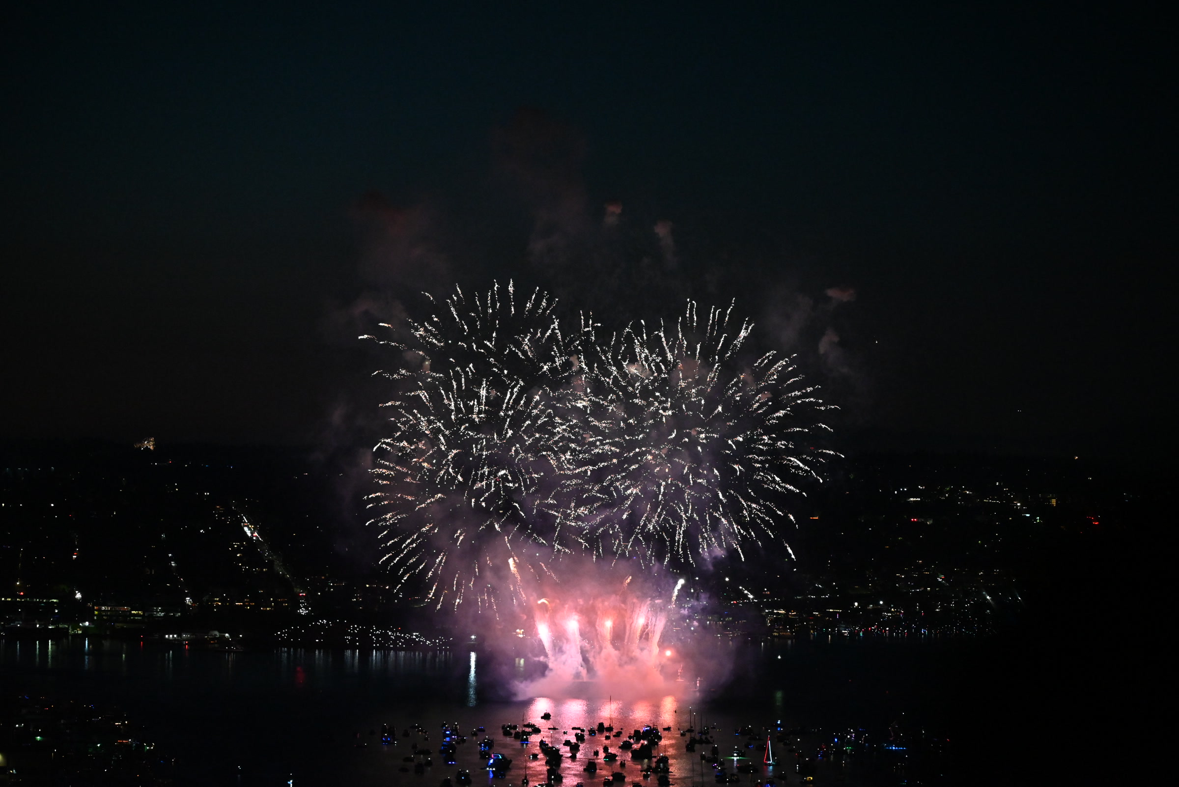 The final pink and white fireworks over boats on Lake Union